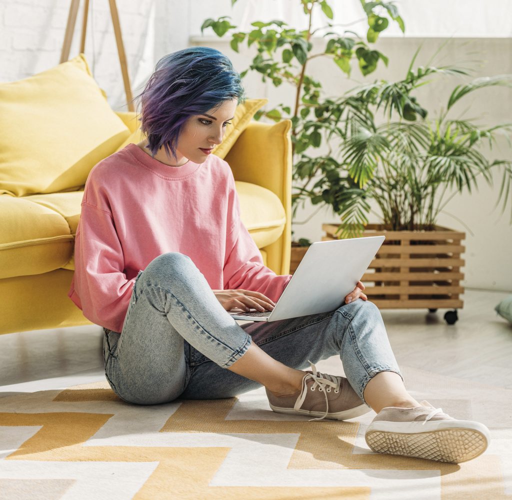 Girl with colorful hair working with laptop on floor in living room