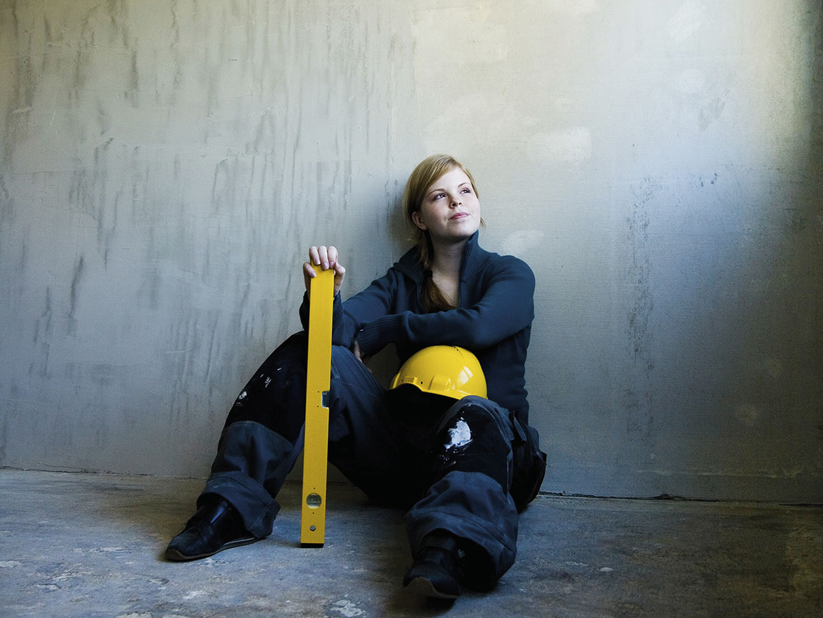 nainen istuu lattialla remonttihaalareissa ja kypärä polvella