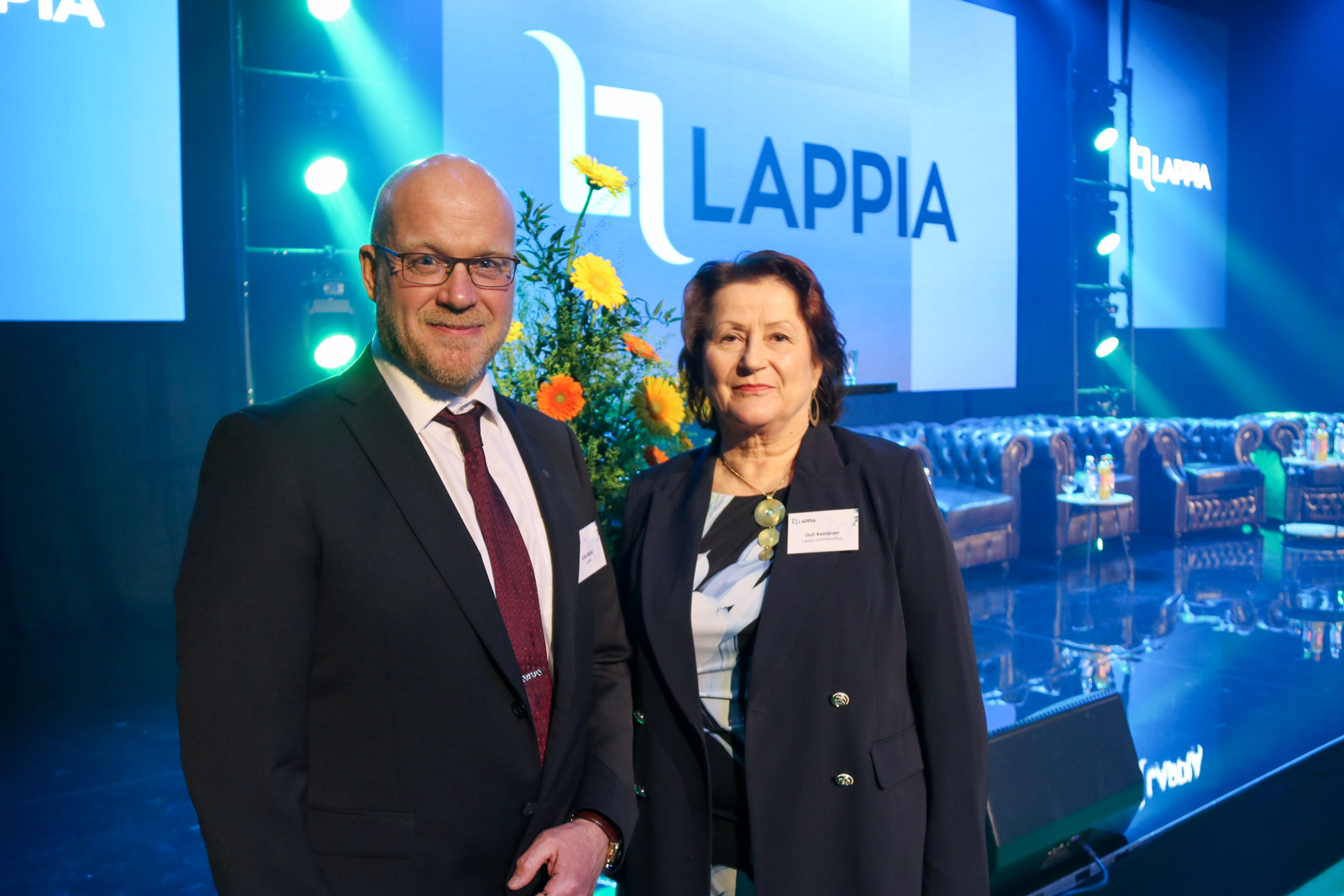 Johtaja Juha Kallo ja yhtymähallituksen puheenjohtaja Outi Keinänen juhlatilassa taustalla kukka-asetelma ja Lappian logo.