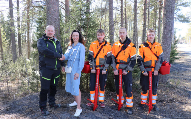 Henkilöt ovat metsän reunassa ryhmäkuvassa.