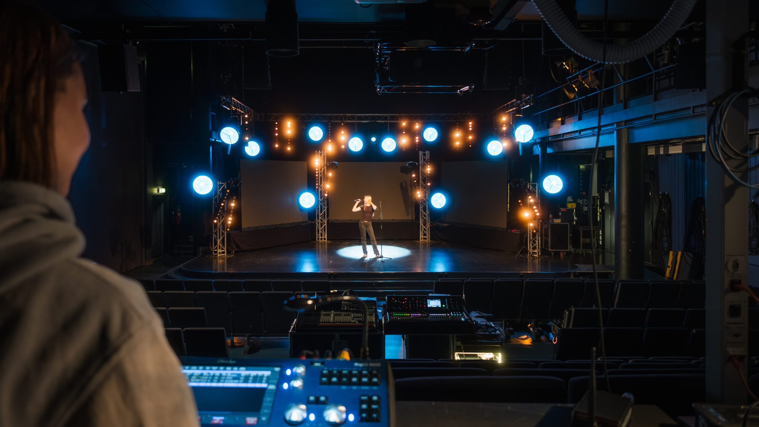 Kuva musiikkitalolta, jossa muusikko on lavalla ja edustalla valopöytä ja sen ohjaaja