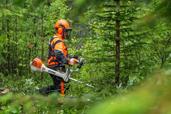 Metsäalan opiskelija raivaussahan kanssa metsässä