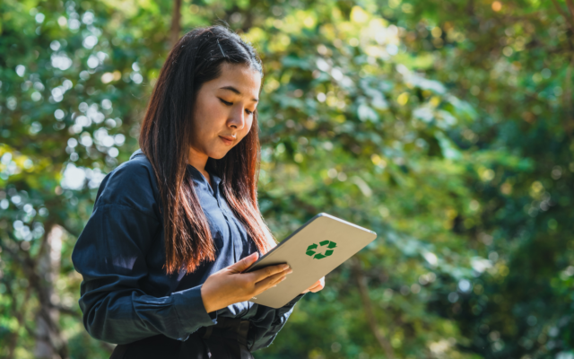 AI4GreenBus-hankkeen uutisoinnin pääkuva, jossa nainen on luonnon keskellä tarkastelemassa kädessään oleva tablettia.