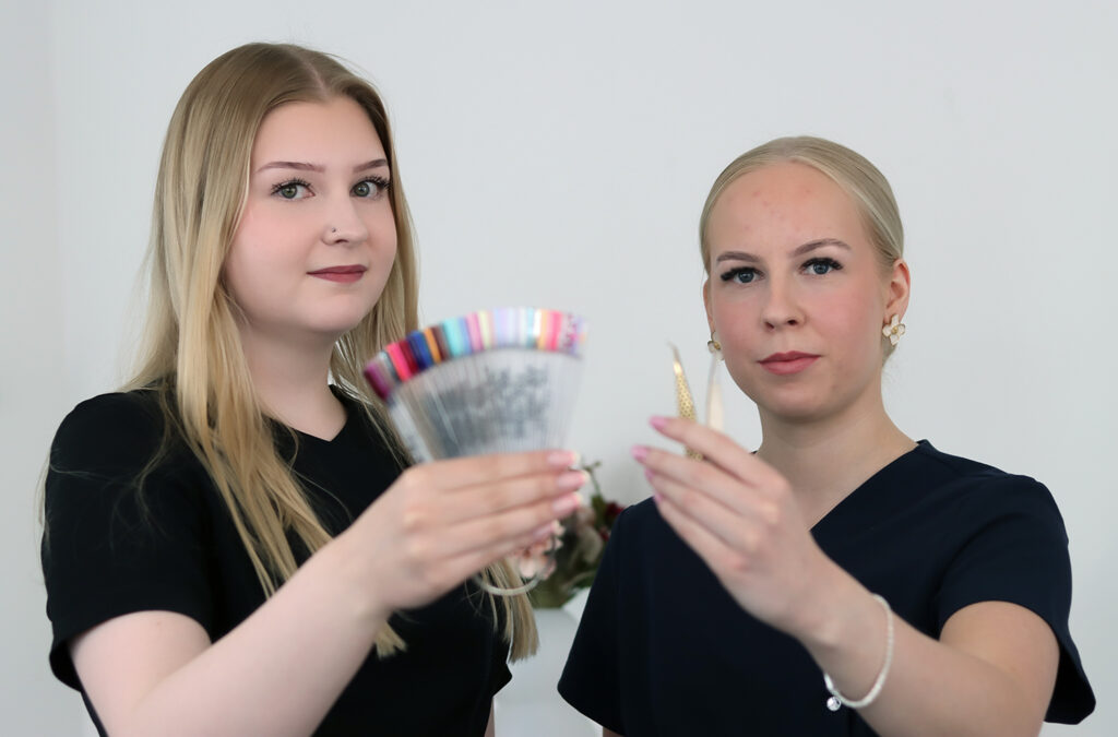 Kuvassa Kauneusstudio Eevan yrittäjät Eerika ja Vanessa esittelemässä kynsiväripalettia ja ripsipinsettejä
